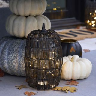A Lit Wire Pumpkin on a front porch in front of other decor.