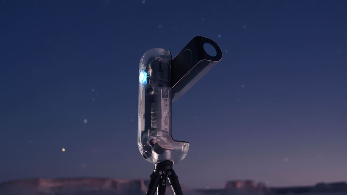 A close-up of the Vaonis Vespera II - X edition showing the clear outer shell and inner workings while pointing at the sky with a starry night sky in the background.