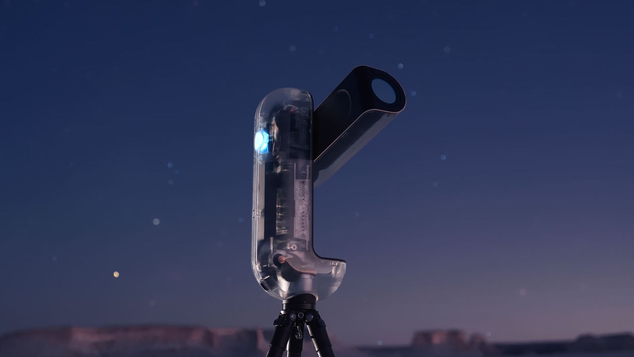 A close-up of the Vaonis Vespera II - X edition showing the clear outer shell and inner workings while pointing at the sky with a starry night sky in the background.
