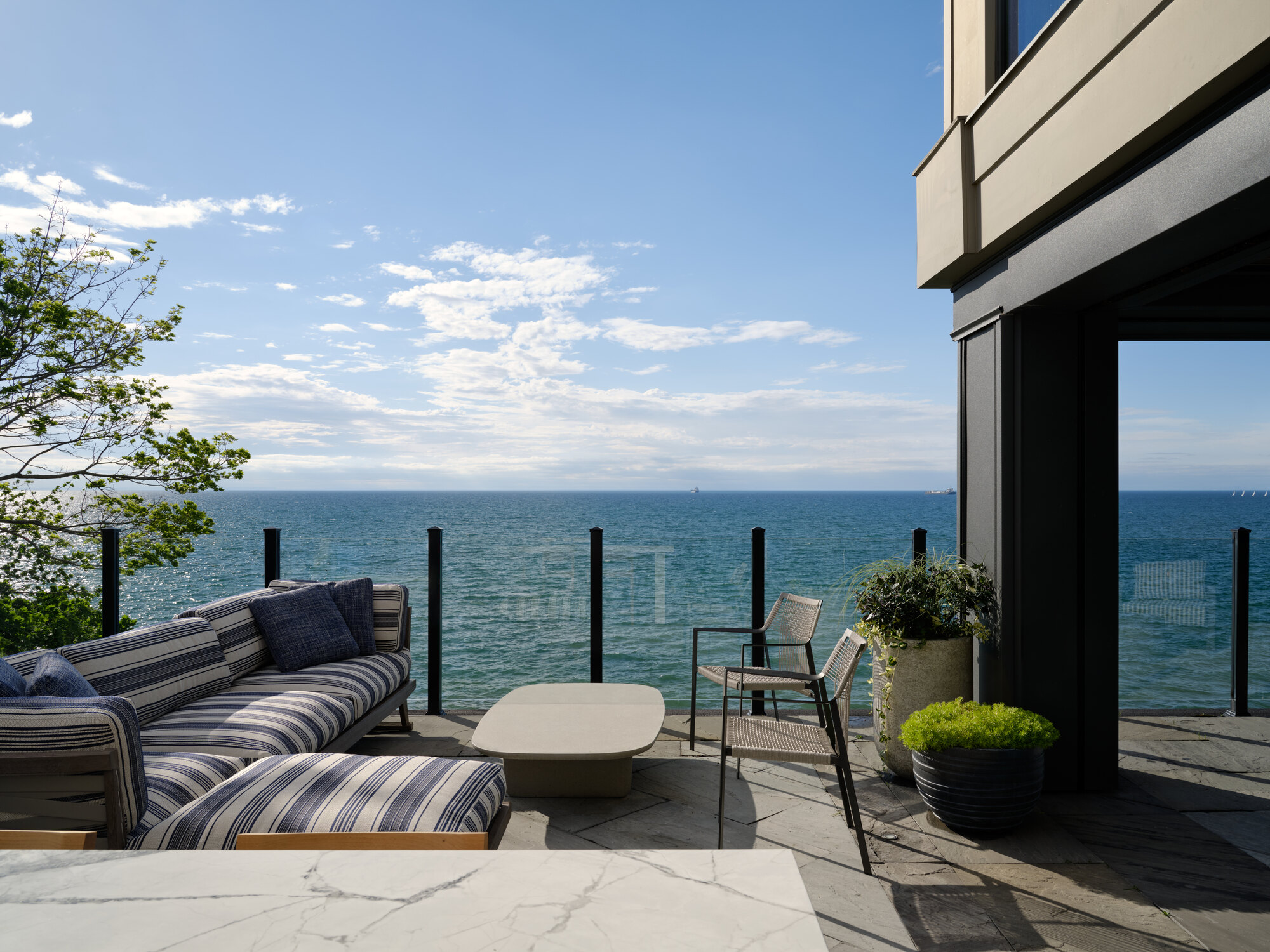 outdoor living area with striped upholstery on sofa, glass balustrade, view of the water, potted plants, and two armchairs