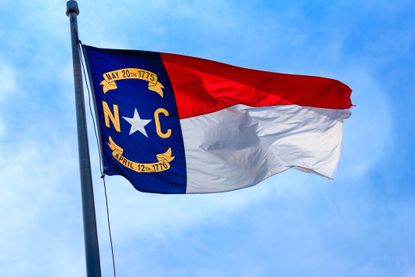 picture of North Carolina state flag on flag pole against blue sky