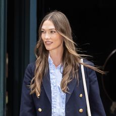 Karlie Kloss wearing a navy blazer over a ruffled blue button-down skirt with a frayed-hem denim midi skirt and brown suede ballet flats.