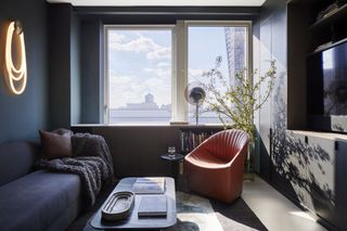 A dark colored couch sits beside a dark blue wall with hanging lighting