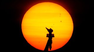 A photo of the sun behind the statue of liberty, with multiple black spots on the sun