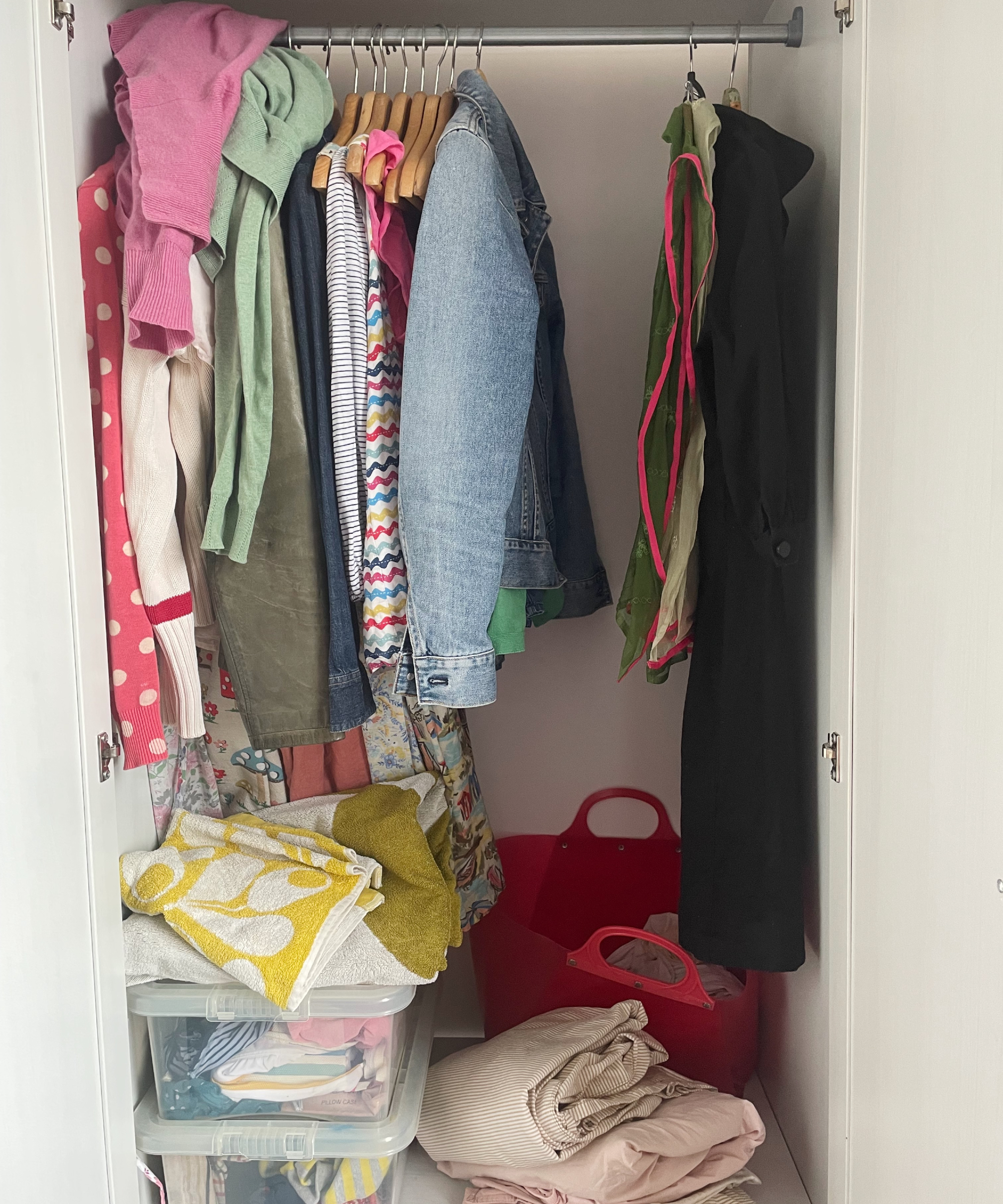 closet showing hanging clothes, clear storage boxes, bedding folded up, red basket