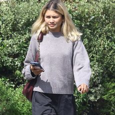 Zendaya walks around Los Feliz California wearing a gray crewneck sweater with black track pants and a Loewe squeeze bag