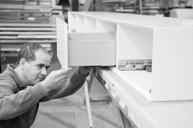 An archive photo. A close-up of a furniture making installing a draw into a cabinet.