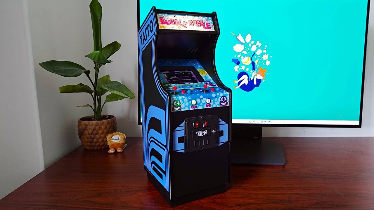 Quarter Arcades Bubble Bobble machine sitting on woodgrain desk with plant and monitor in backdrop.