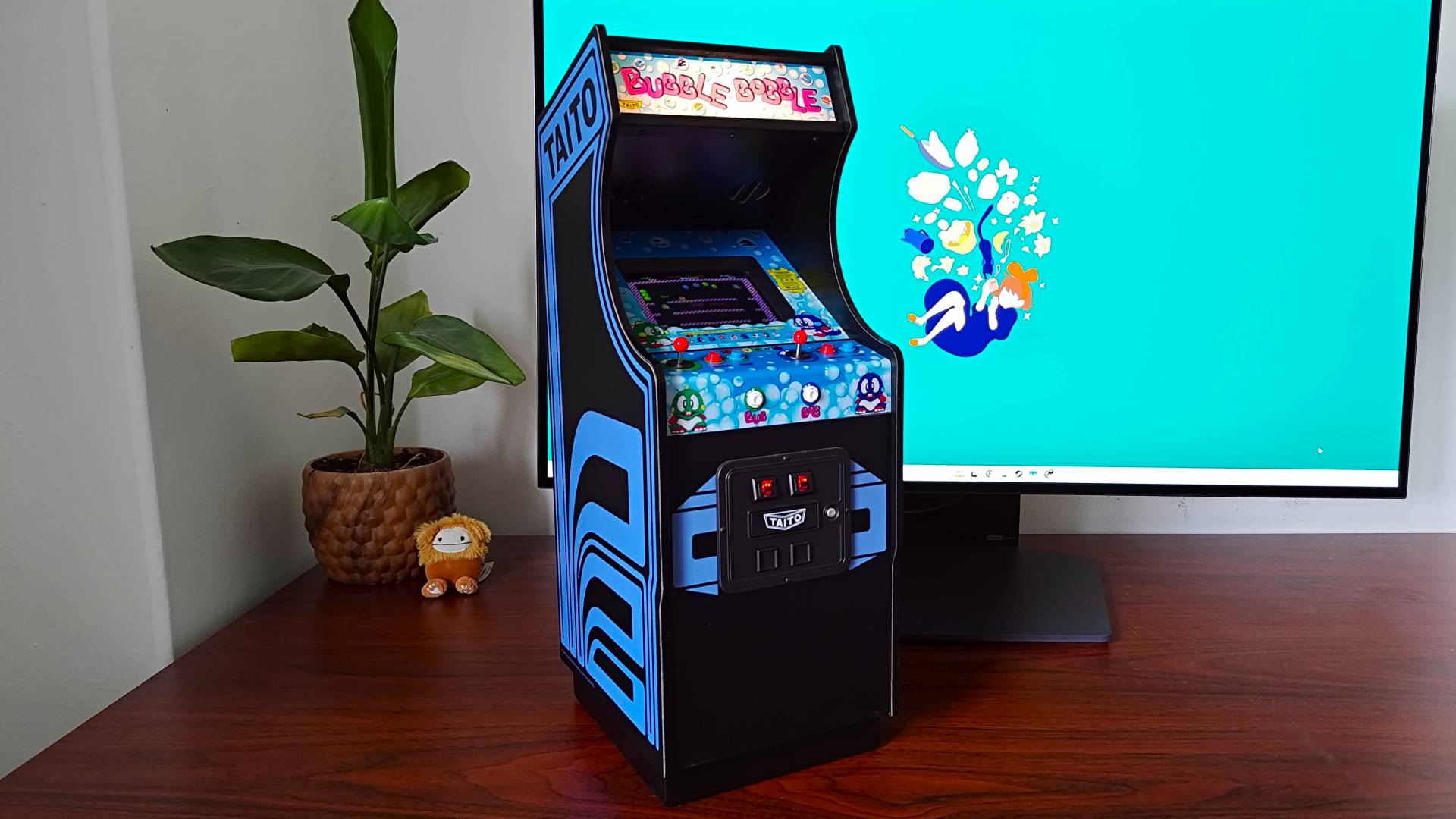 Quarter Arcades Bubble Bobble machine sitting on woodgrain desk with plant and monitor in backdrop.