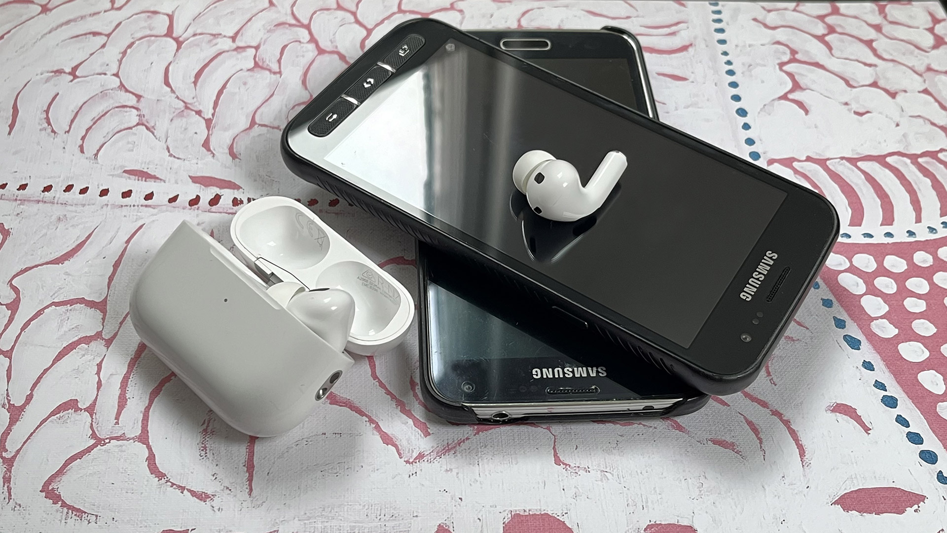 A pair of AirPods sit on top of two stacked Samsung phones