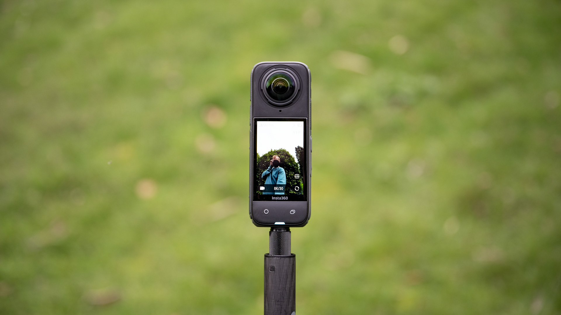 Insta360 X4 360 degree camera outdoors with vibrant grassy background, recording video