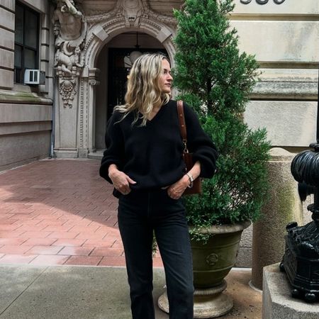 Eliza Huber wearing a black V-neck sweater, brown bag, black Citizens of Humanity Zurie black jeans, and brown shoes.