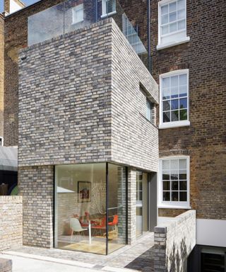 narrow light grey and stone brick extension with corner glass wall on ground floor