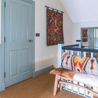 Bench with ikat pillow on landing with sisal floors, white walls and blue-green doors and skirting boards