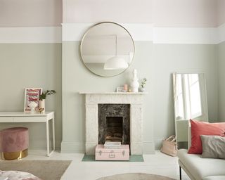 A living room paint idea by Dulux with muted pastel green paint and pastel pink paint on ceilings, white furniture, and a white fireplace with a mirror above it