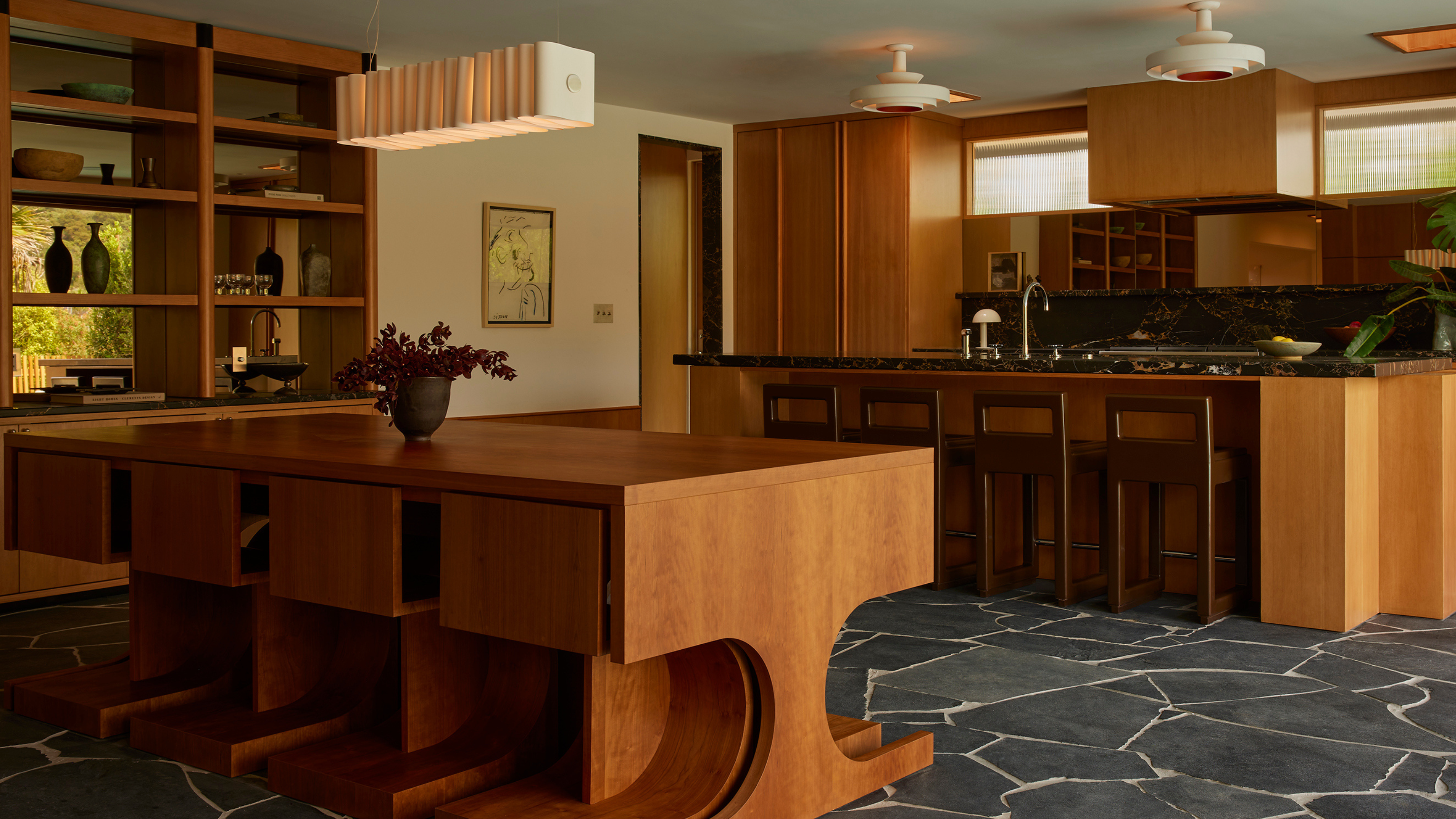 mid-century kitchen design with wooden features, a stone floor, and a sculptural dining table at the centre