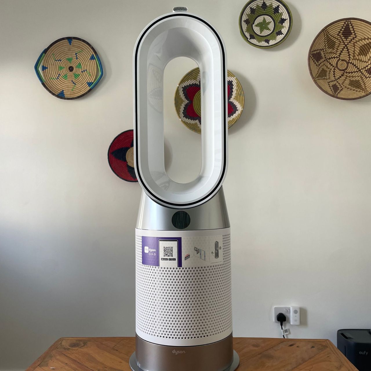 Dyson Purifier Hot+Cool HP1 Purifying Fan Heater sitting on a wooden table in front of a white painted wall with colourful baskets on it
