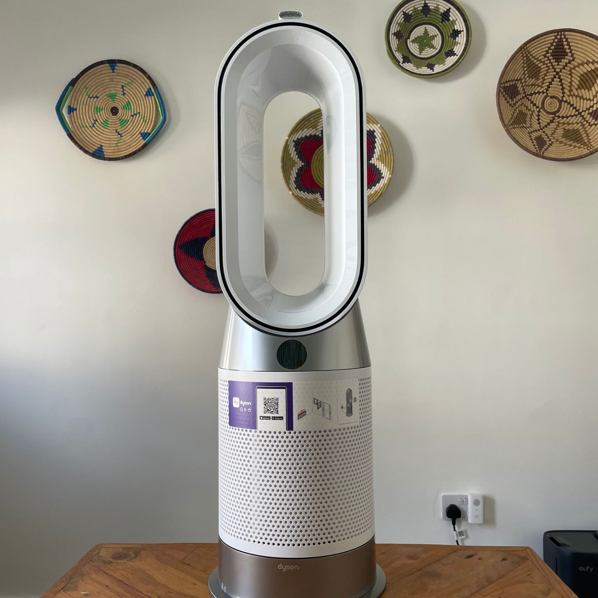 Dyson Purifier Hot+Cool HP1 Purifying Fan Heater sitting on a wooden table in front of a white painted wall with colourful baskets on it