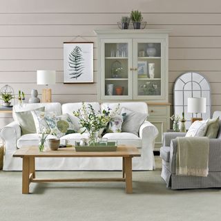 neutral living room with horizontal wall panels, a white sofa with white and green cushions, a green display unit with brown trimmings and a wooden coffee table
