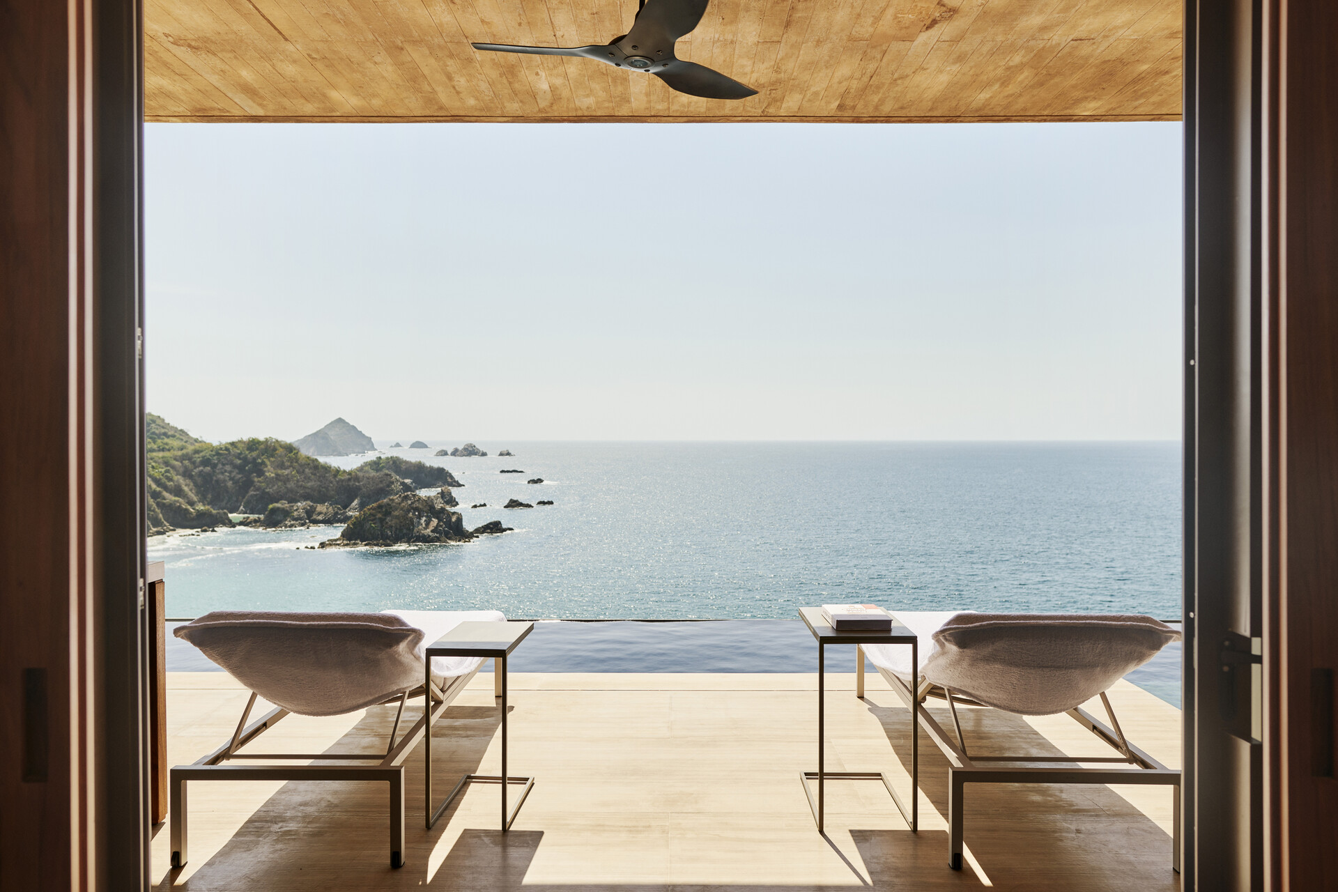 view from a suite at four seasons tamarindo resort showing two sun loungers facing a private infinity pool with the pacific ocean behind on a sunny day