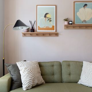 A dove grey-painted living room with a green sofa and art prints displayed on floating shelves