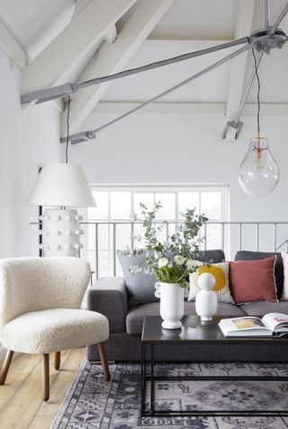 Living aroom wih gray couch, armchair and coffee table with pendant light over and vaulted ceiling in white and white walls