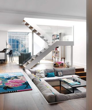 All white basement living room, sunken sofa, central staircase.