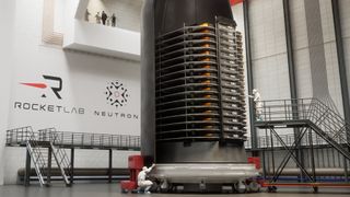 A stack of thin satellites sits in half a rocket fairing in a clean room. 