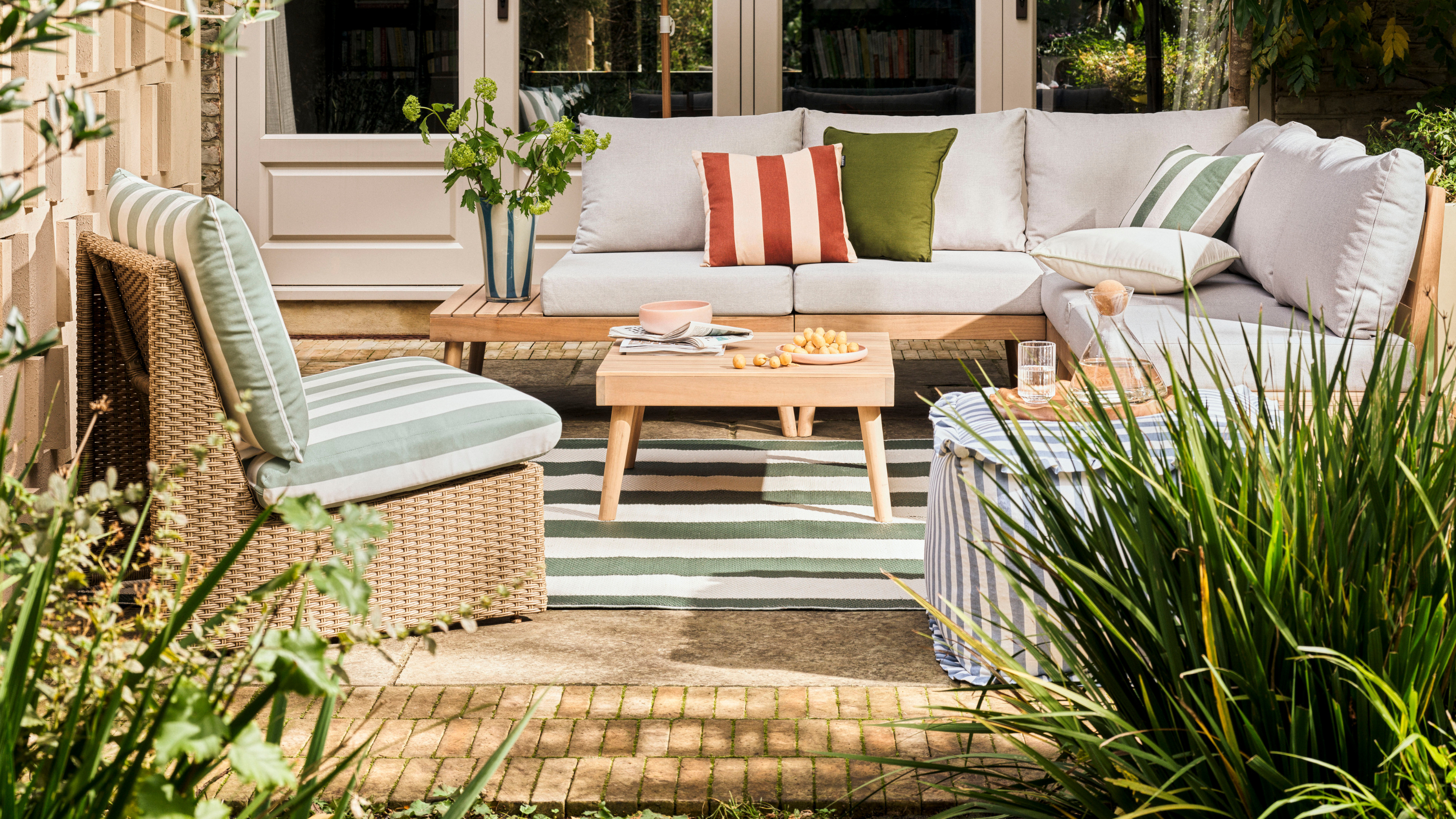 Habitat striped outdtoo pouffe on a patio next to green striped rug, green striped accent chair and sofa.