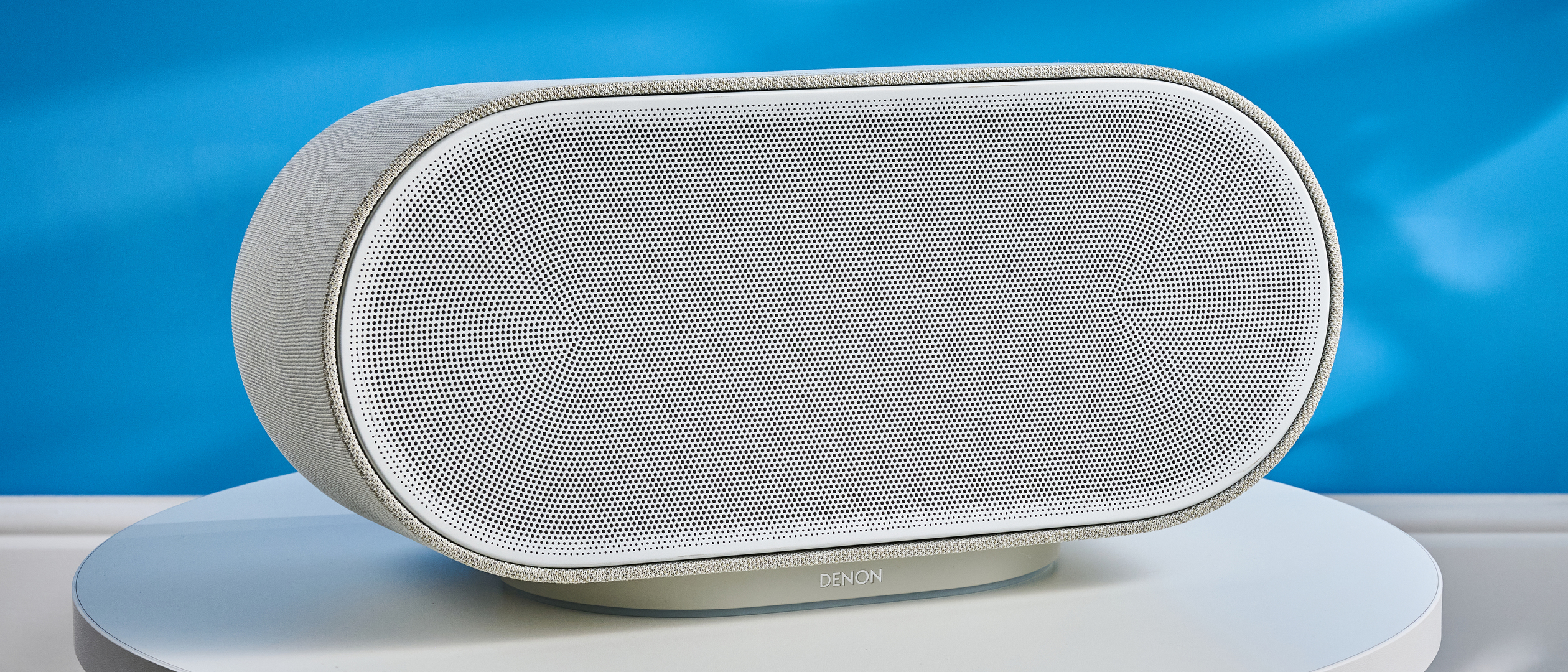 the denon home 600 home speaker in stone color photographed against the blue tom's guide background