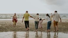 Multigenerational family members walk on the beach, some of them holding hands.
