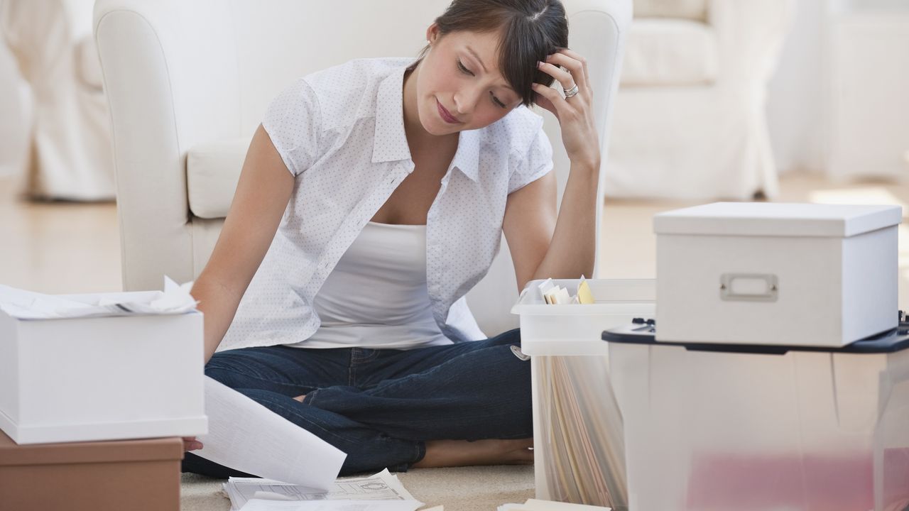 A woman sits on the floor surrounded by boxes of paperwork.