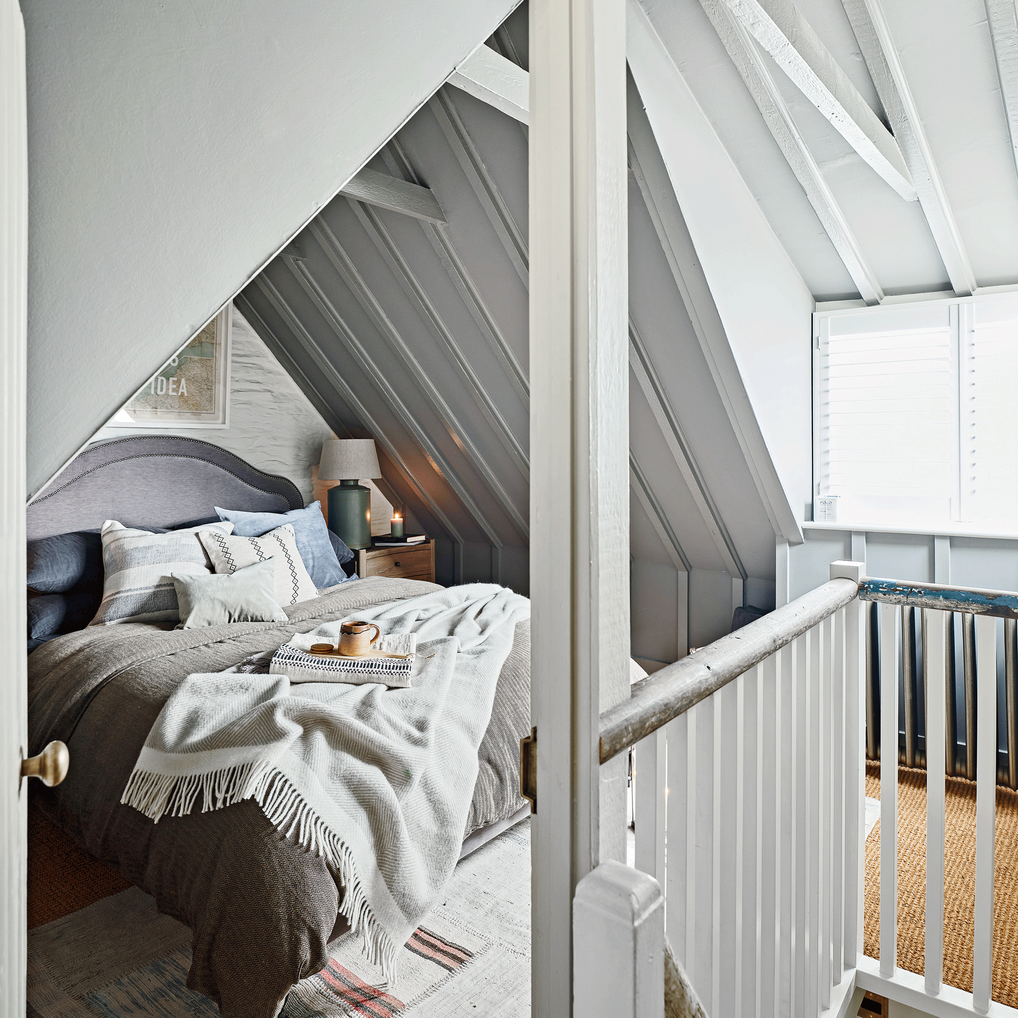a cosy bedroom in a loft room with sloping walls and a staircase and bannister in the foreground
