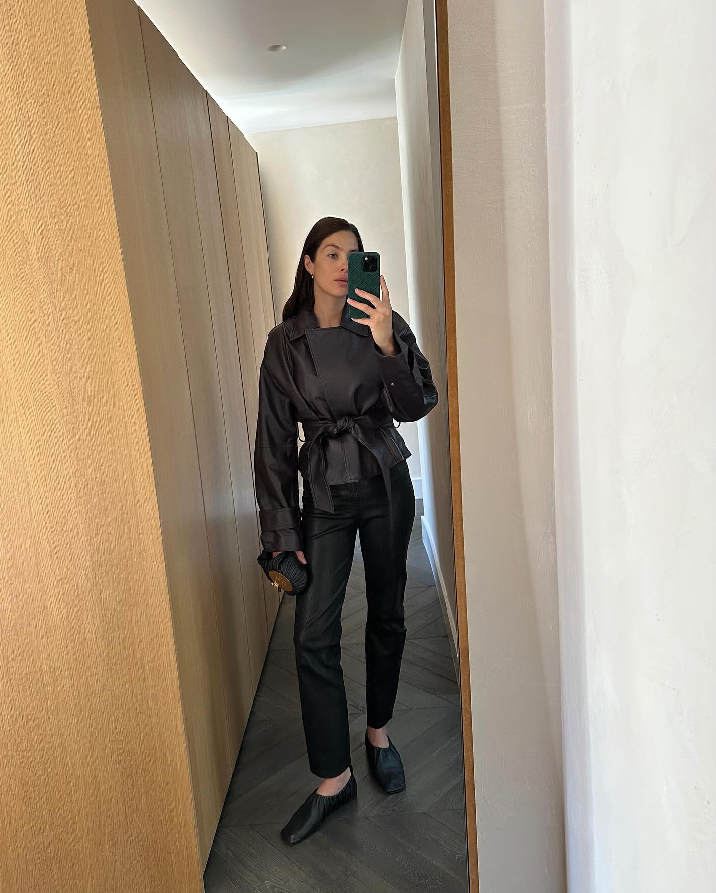 Woman wears black cigarette pants, a leather wrap coat and square toe flats.