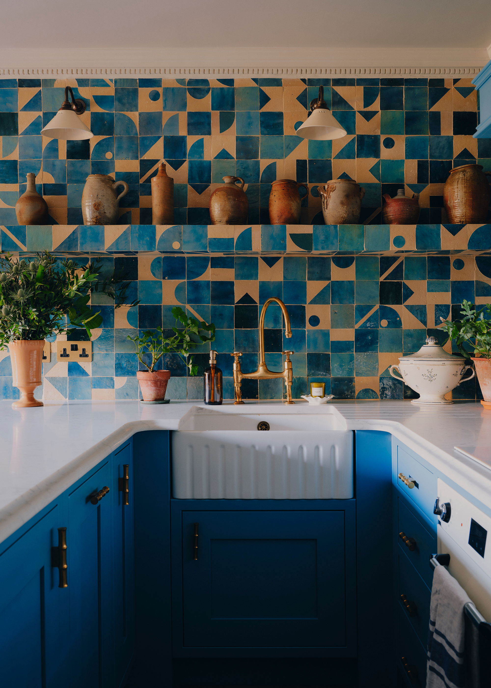 A modern traditional bright blue kitchen with boldy pattern tiles for the backsplash and a built in shelf mid way up to the ceiling, also tiled