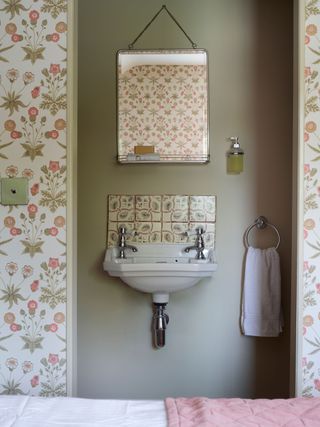ensuite bathroom doorway with floral wallpaper around and small basin leaf patterned splashback and green walls
