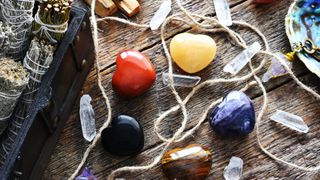 Types of crystals for your star sign: A top view image of several heart shaped healing crystals with white sage smudge sticks and clear quartz crystals on a dark wooden table top.