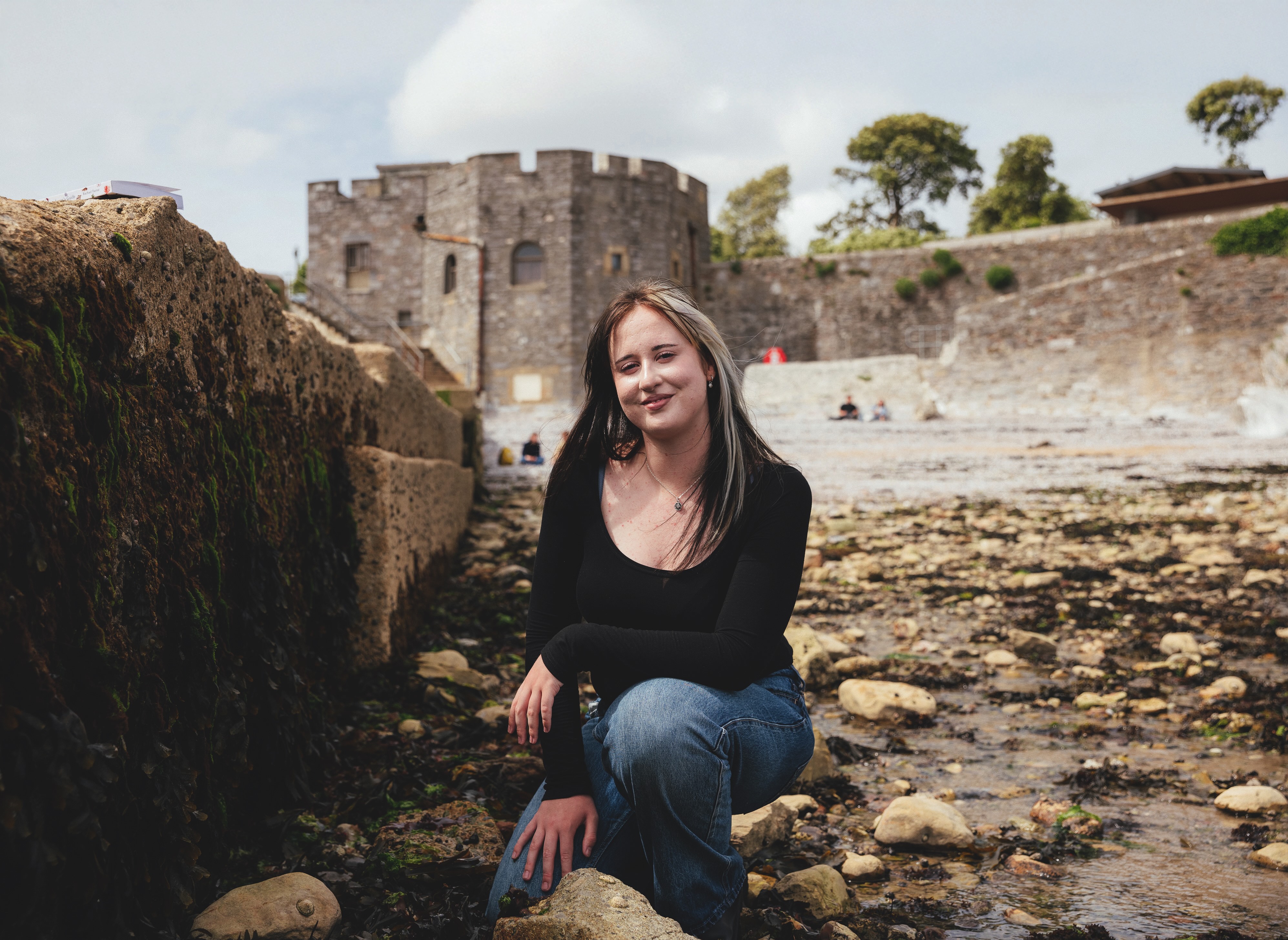 Emma Stoner kneels on a rocky foreshore looking at the camera