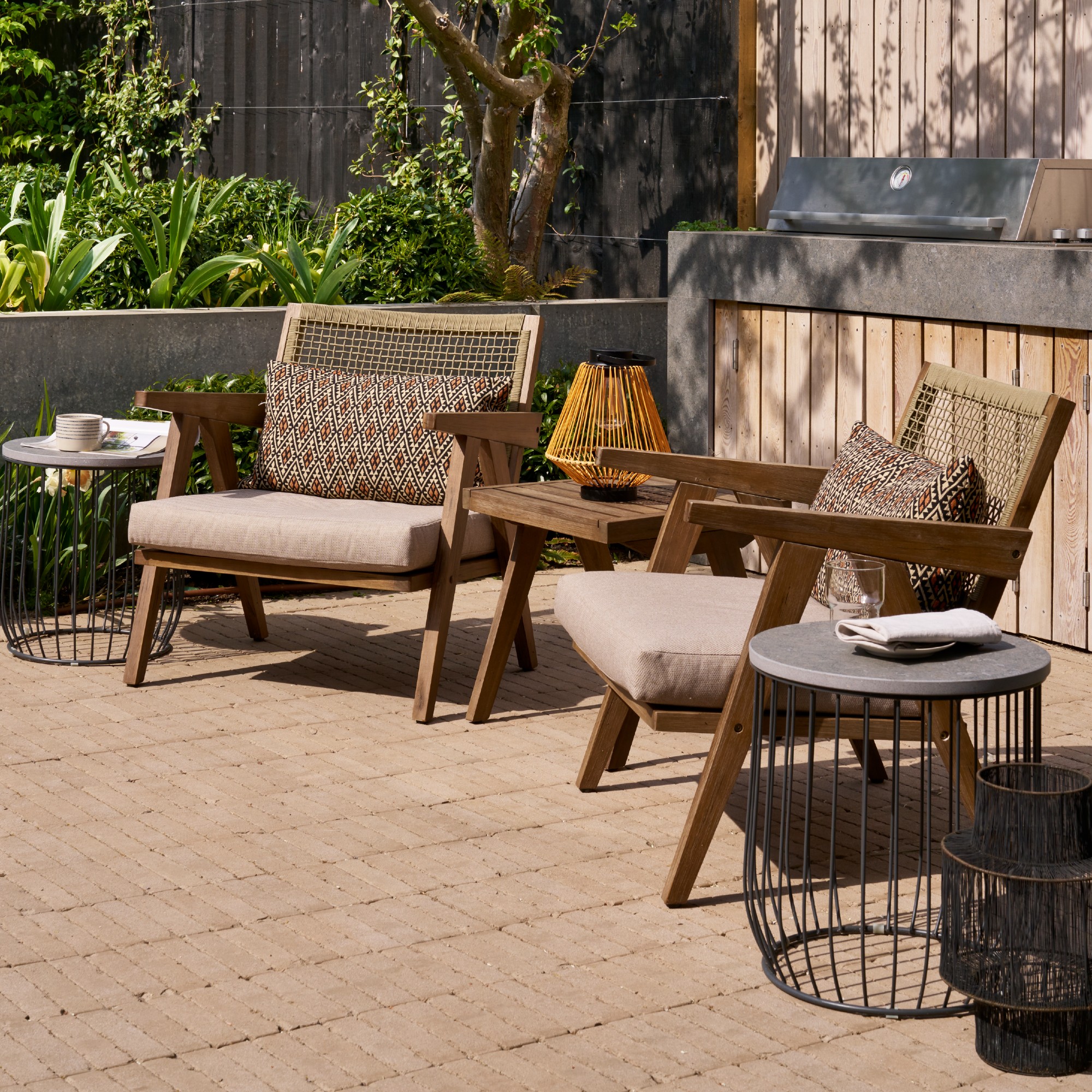 A patio with two wooden lounge chair and a coordinating side table in the middle with two metal side tables on either side