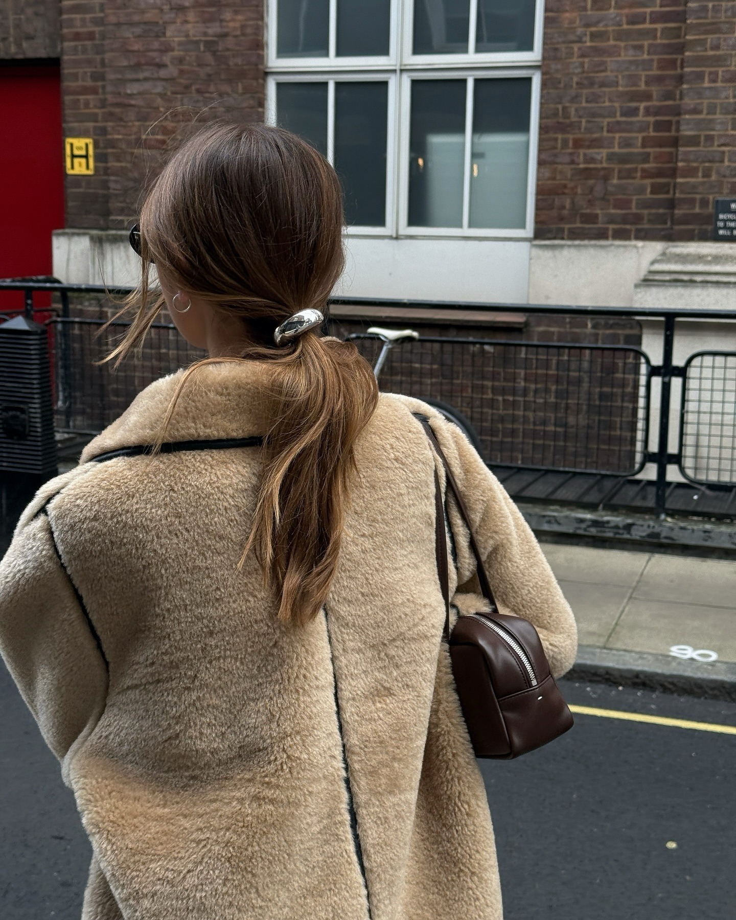 A woman wearing a shearling coat with a ponytail and a metal silver hair tie