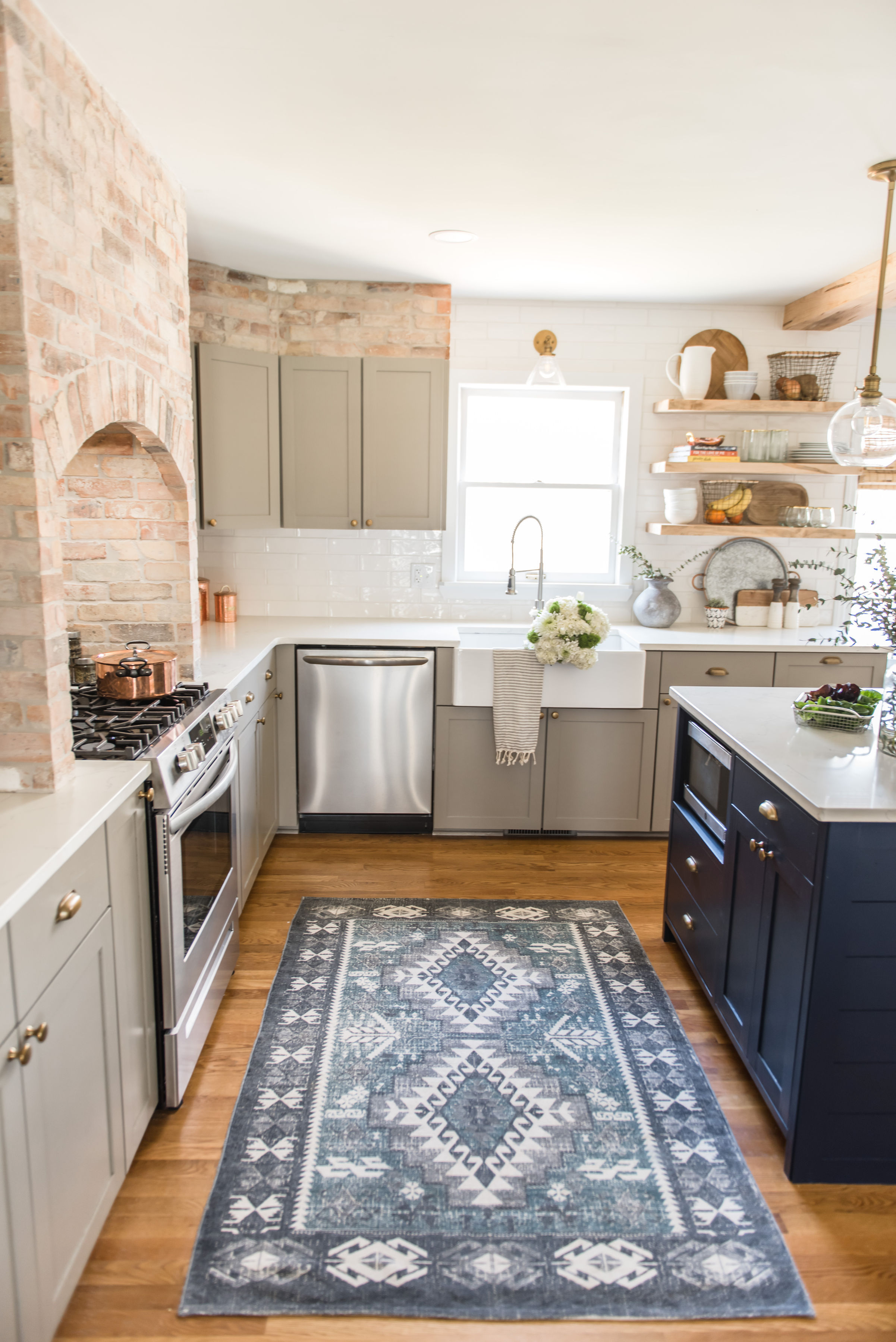 Painted kitchen cabinet ideas in pale stone gray and midnight blue in a rustic kitchen with wooden flooring and exposed brick walls.