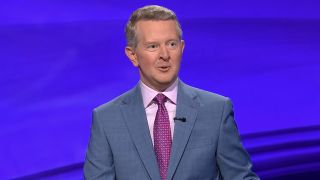 Ken Jennings in gray suit with pink shirt and magenta tie hosting Jeopardy! 