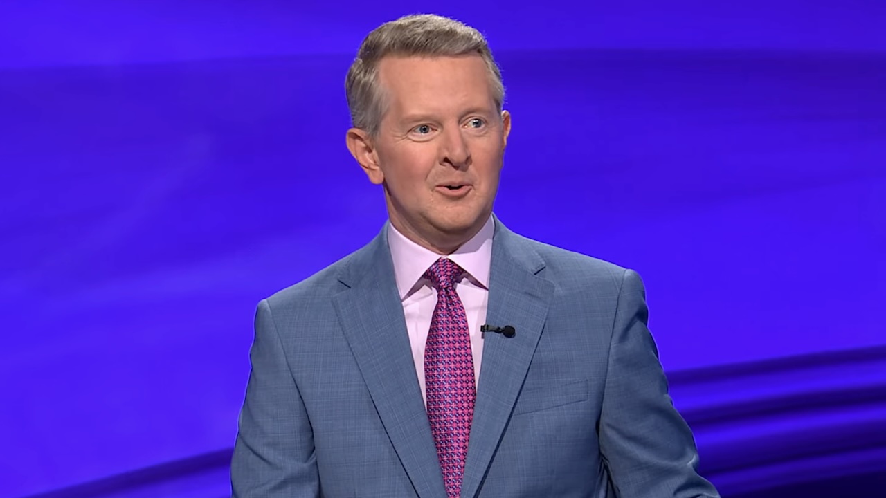 Ken Jennings in gray suit with pink shirt and magenta tie hosting Jeopardy! 