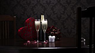 Two champagne glasses and a heart full of candy on an intimate table setting for Valentine's Day.