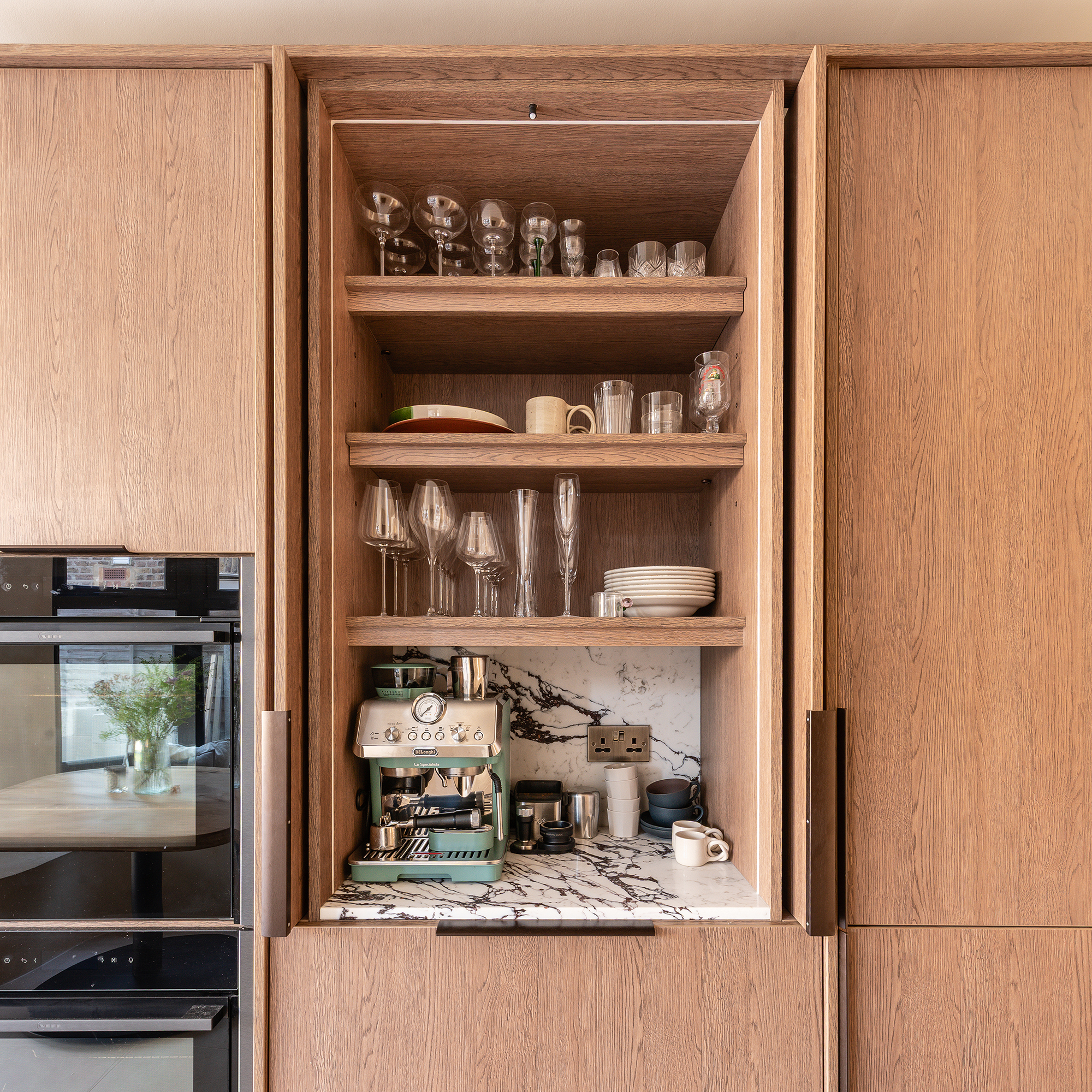 Light wood kitchen showing hidden pantry with marble worktop and shelves for plates and glassware