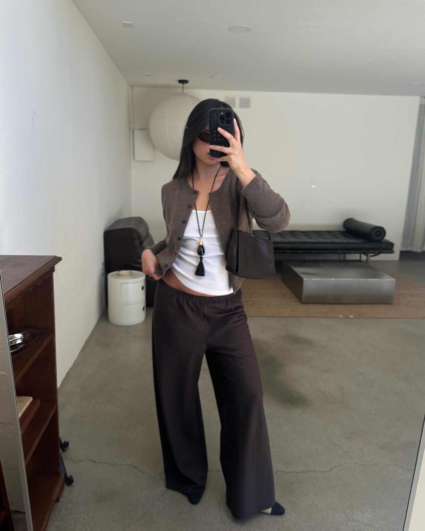 Woman in a cardigan, tank top, pants, and a pendant necklace.