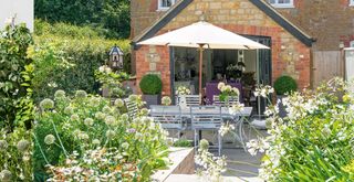 cottage garden idea with cream planting surrounding a dining area with a cream parasol