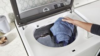 person loading blue towel into the Maytag MVW7232HW top load washer