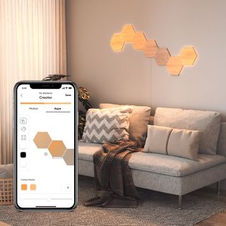 Nanoleaf Elements Hexagons mounted on a wall in a living room setting with Nanoleaf app displayed on a phone