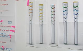 White wall, pictures of different inner colour variations of the Olympic torch, written notes and paper markers to the left of the shot